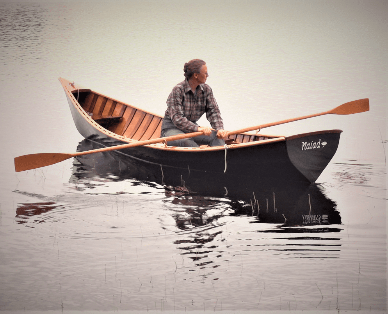 Man rowing a small wooden boat on calm water.