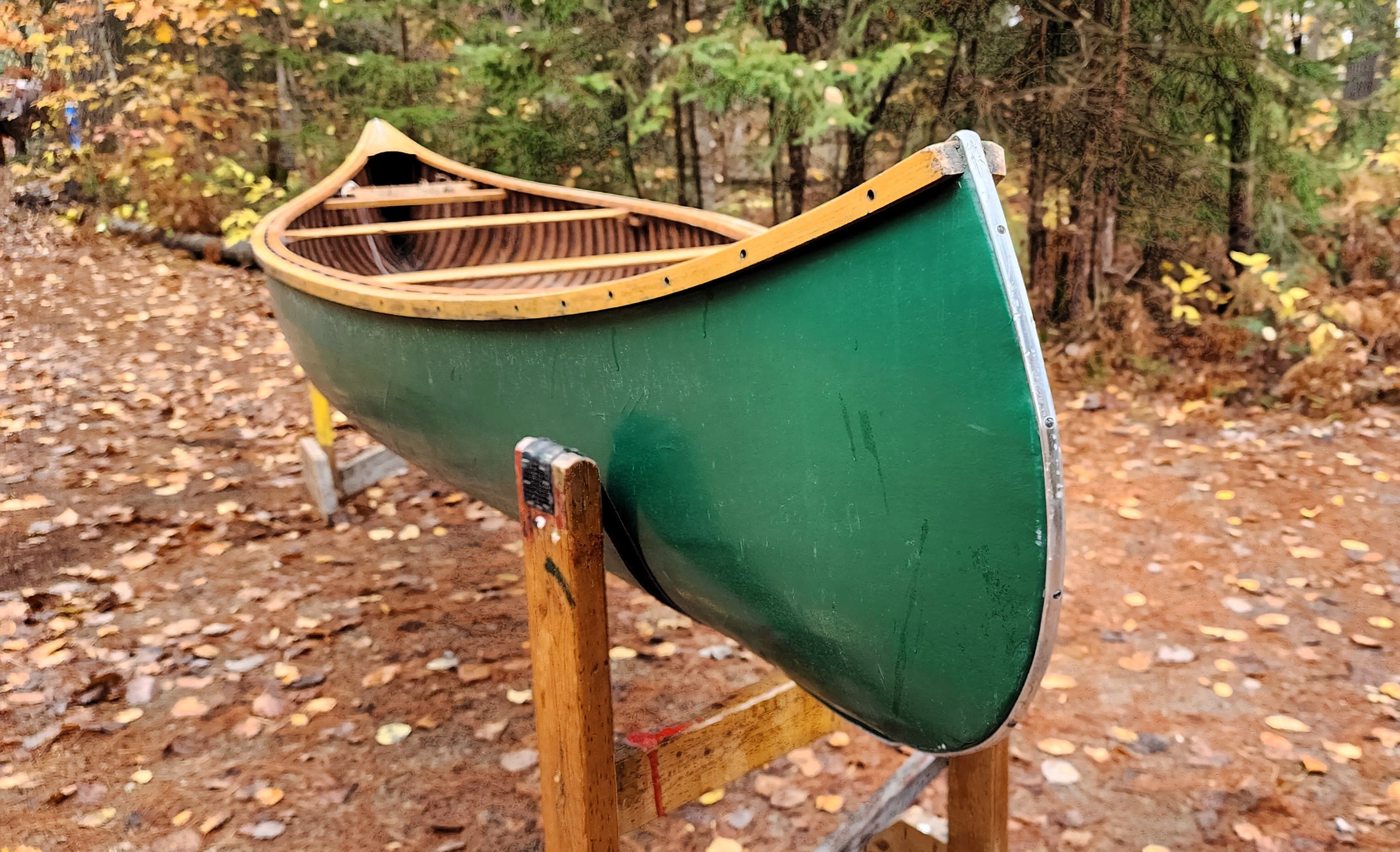 Green canoe resting on a wooden stand outdoors.