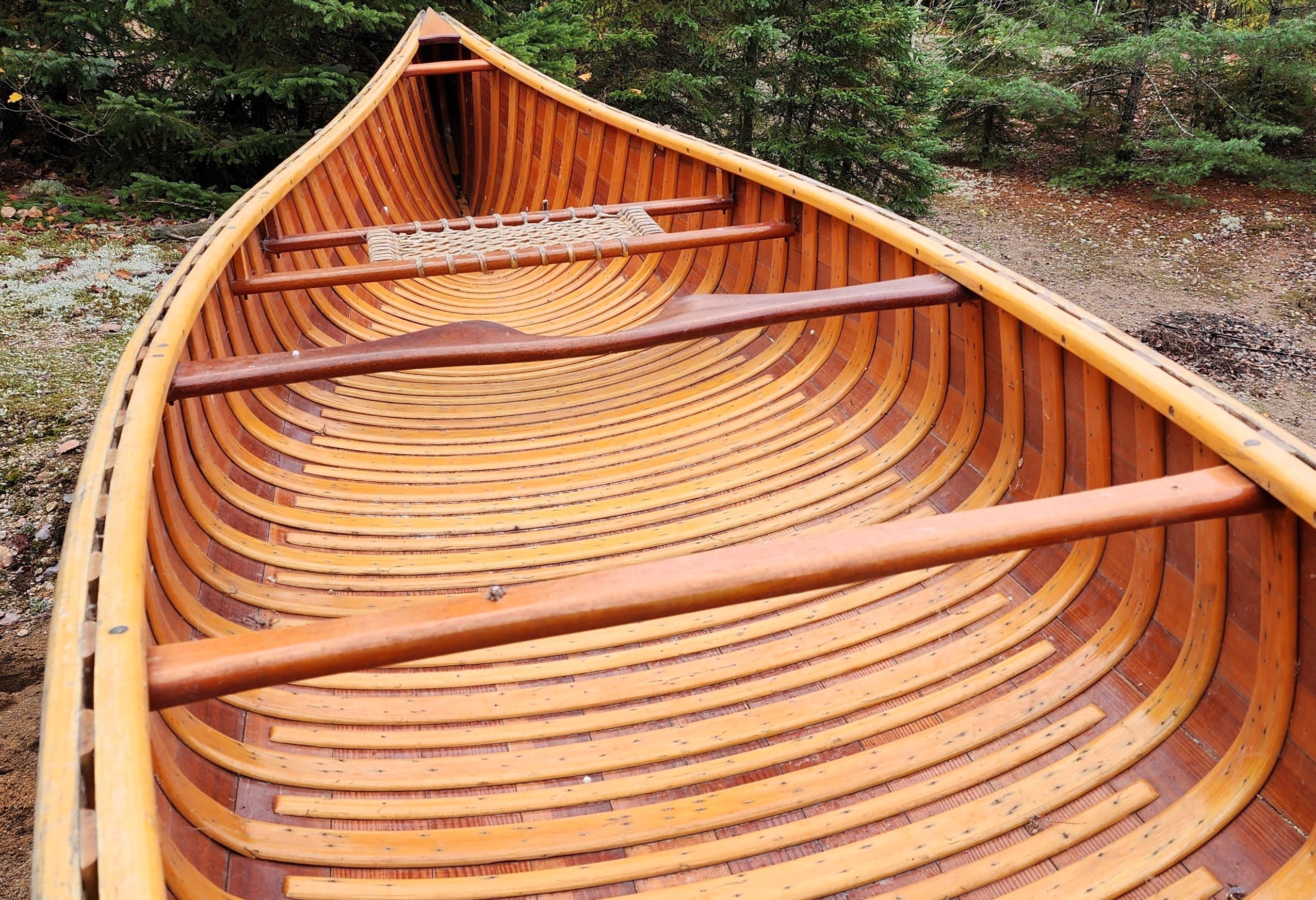 Wooden canoe with detailed ribbing inside, set outdoors.