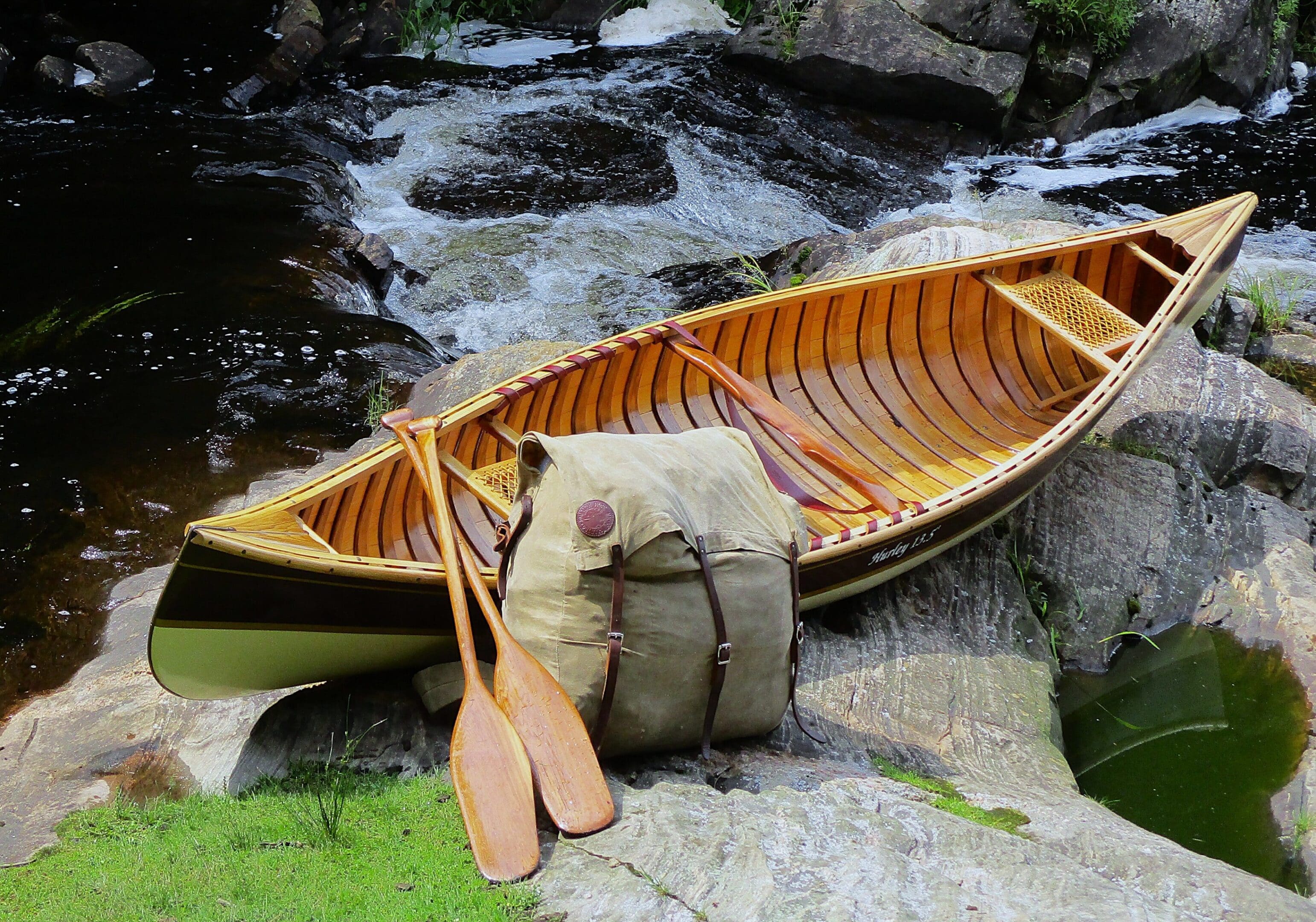 Wooden canoe and paddles resting by a rocky stream.
